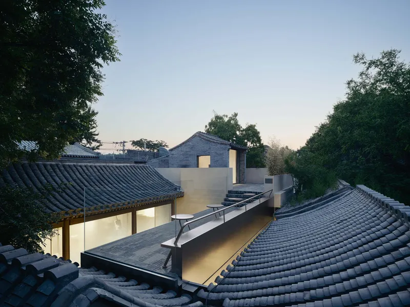 Rooftop view at twilight showing curved tile roofs surrounding white volumes and glass skylight