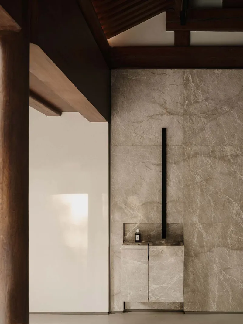 This architectural image showcases a minimalist bathroom design with a focus on natural materials and clean lines. The space features a marble wall and cabinet,