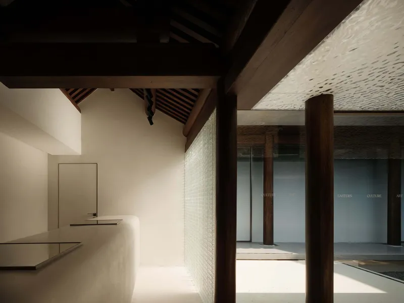 Interior view through timber columns toward a glazed courtyard with reception desk and perforated ceiling