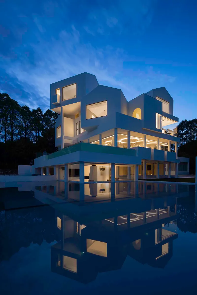 Sculptural white facade reflected in still water at twilight with glowing interior lights