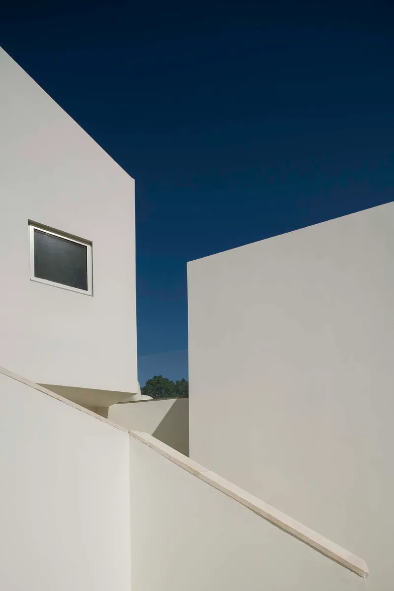 Upward view of white rendered walls meeting at an angular corner against a deep blue sky