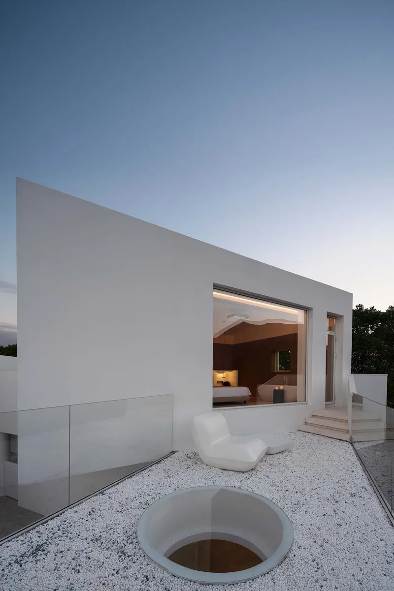Terrace with white gravel and circular skylight opening framed by white walls at dusk