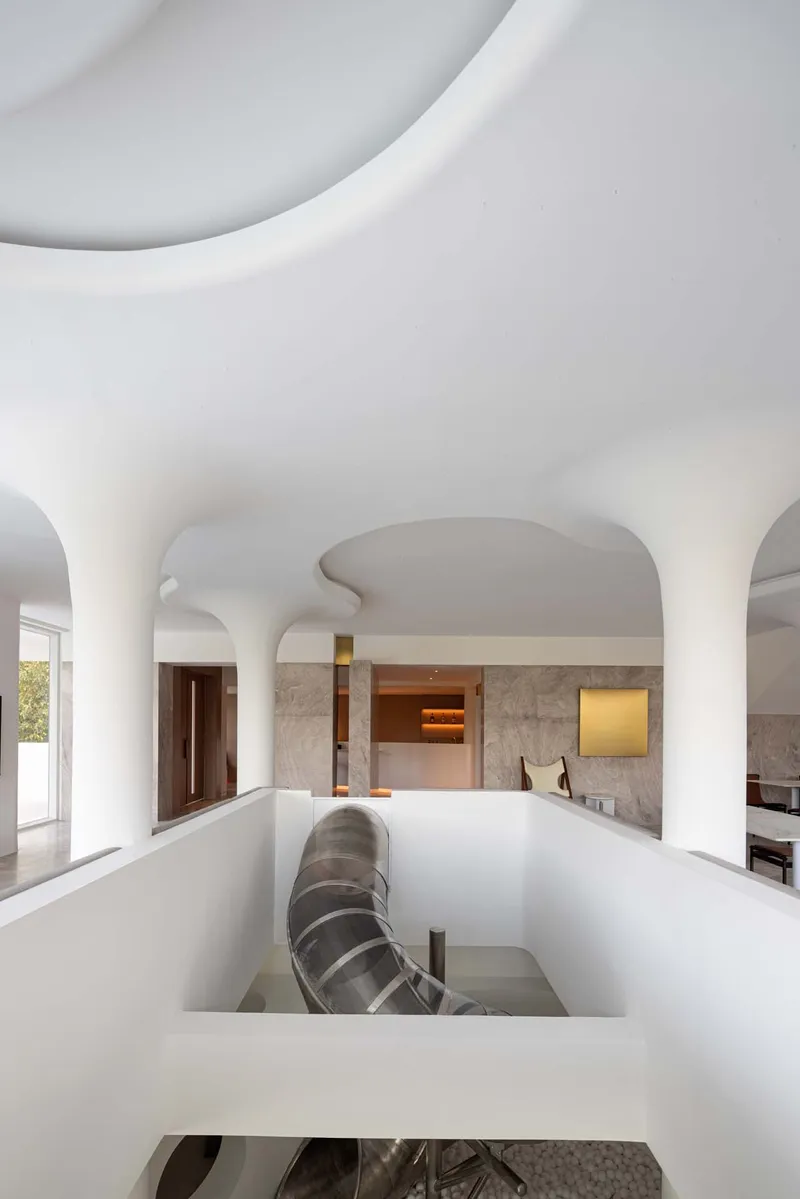 Interior view through sculptural white ceiling opening revealing upper level with stone walls and timber doors