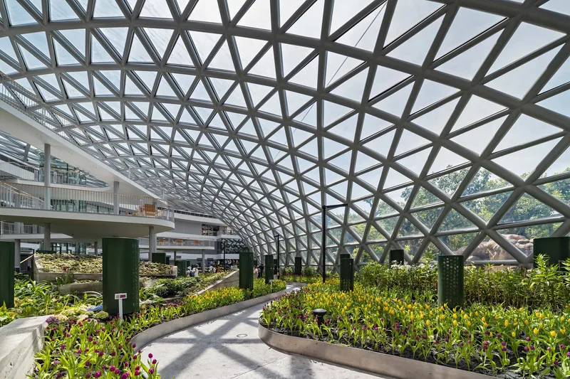 Covered garden terrace with diagonal steel roof structure sheltering planted beds and walking paths