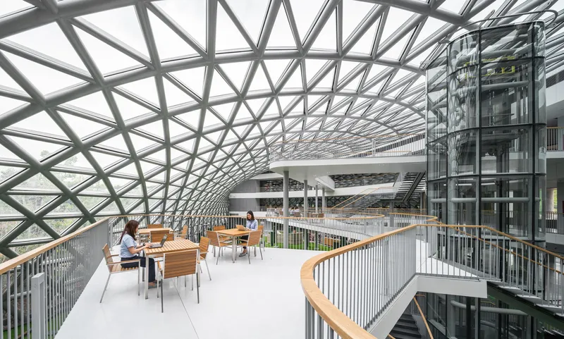 Multi-level atrium with curved steel lattice roof and balconies overlooking a central study space