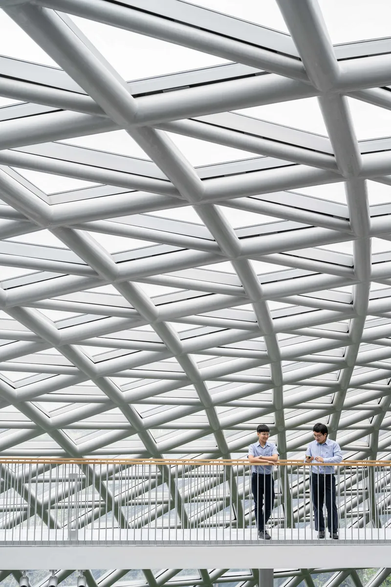 Two figures on a bridge beneath a curving diagrid steel roof canopy