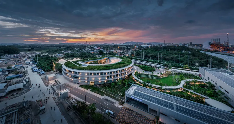 Aerial view of circular building with planted roof terrace at sunset