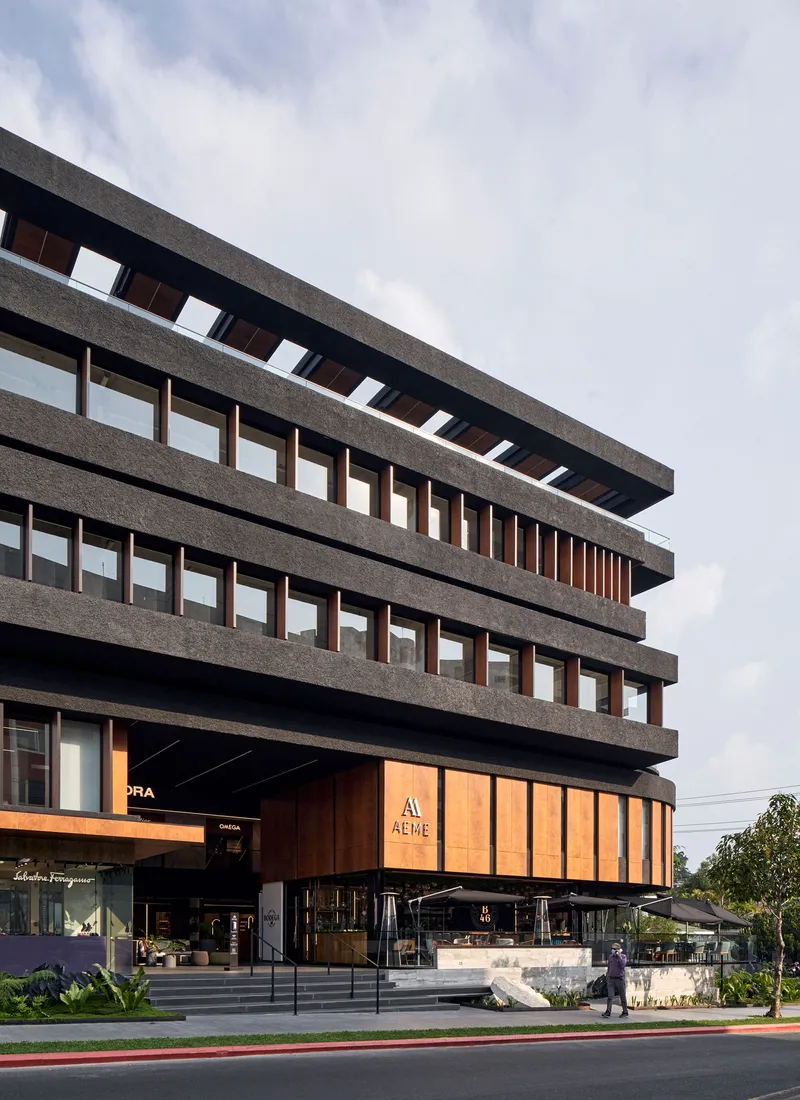 Street view of the layered concrete facade with horizontal bands and timber-clad ground floor shopfronts