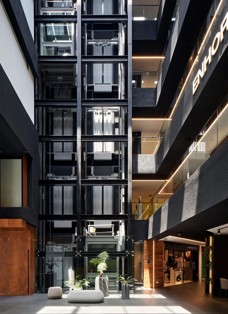 Interior atrium with exposed glazed elevators and planted planters on a white tile floor