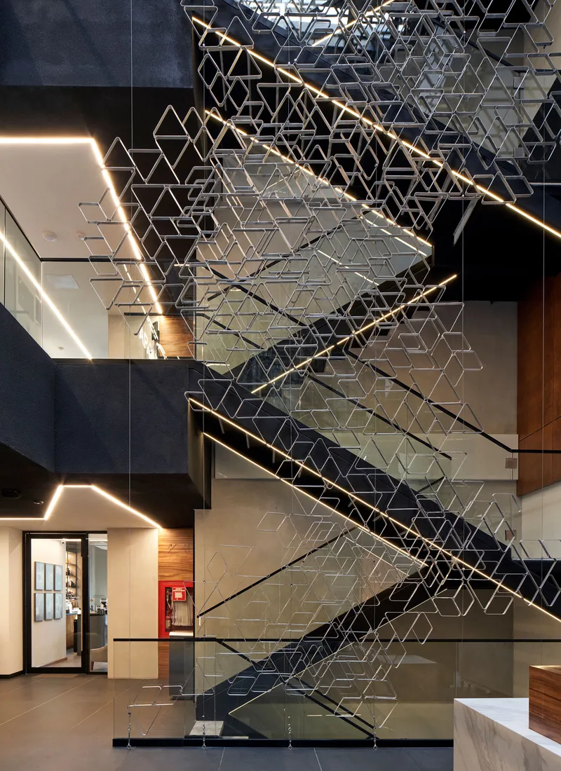 Sculptural metal screen wrapping the staircase in a multi-level lobby with linear ceiling lighting