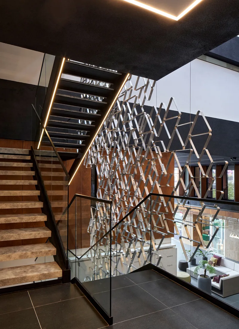 Timber staircase alongside the perforated metal screen with glass balustrade and recessed ceiling lighting