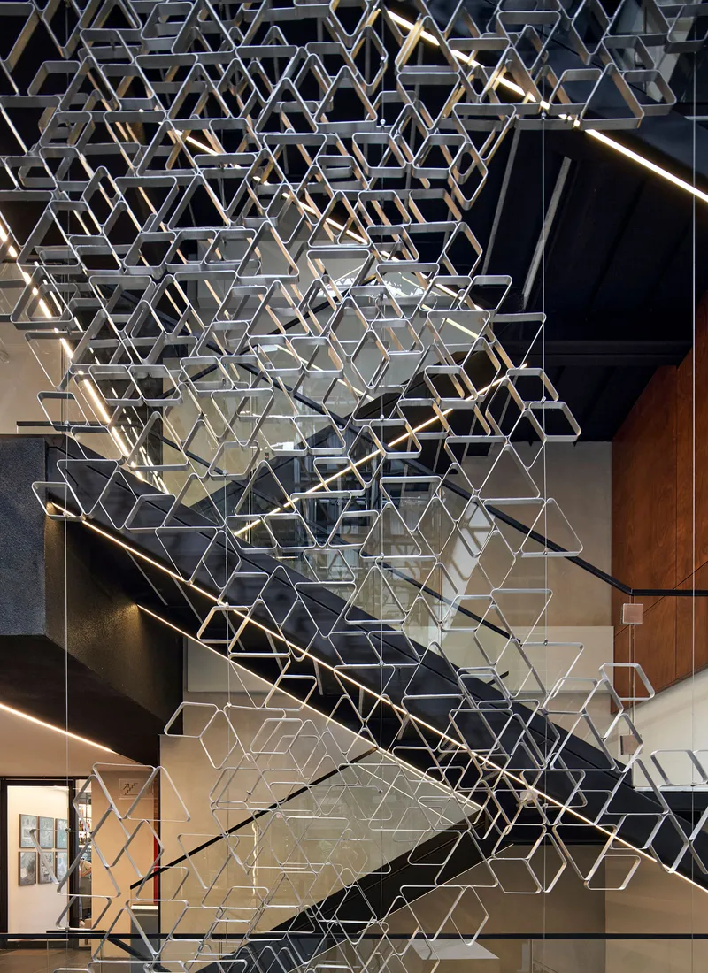 Suspended hexagonal metal screen hanging above a staircase with linear lighting on the treads