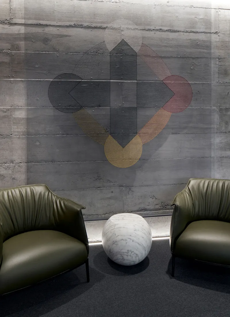 Concrete wall with geometric artwork above two green leather chairs and a marble side table
