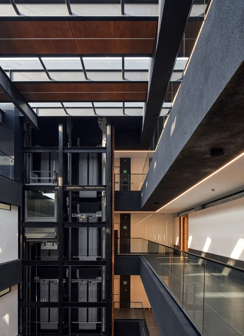 Interior atrium with exposed glass elevator shaft and timber ceiling panels in bright daylight