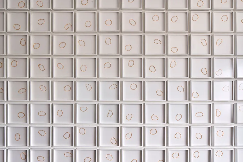 White grid wall panel with copper wire loops set into each recessed square cell