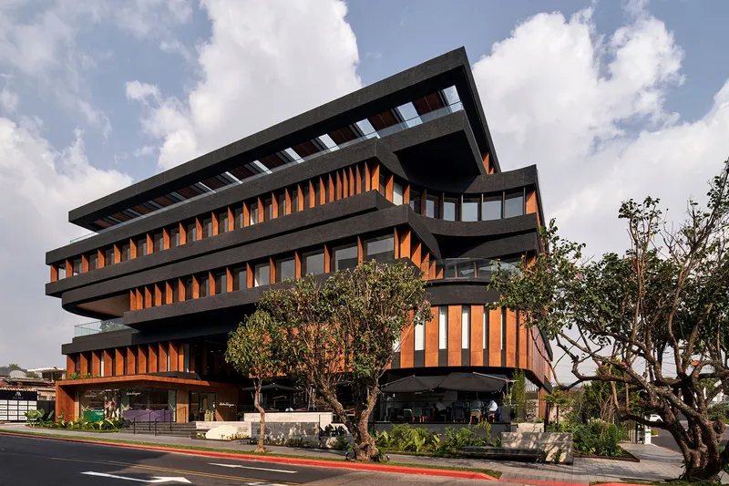 Corner view of the cantilevered floors with timber louvers and mature trees in the foreground at dusk