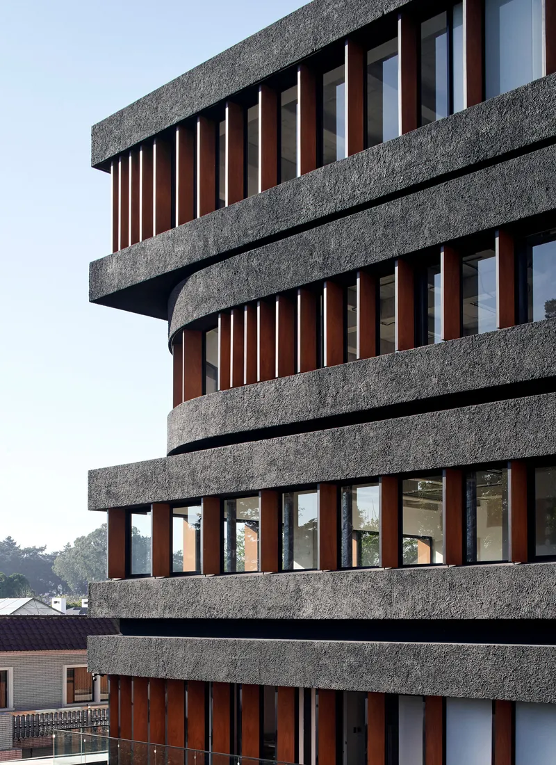 Close-up of the textured concrete slabs alternating with vertical timber fins wrapping the curved facade
