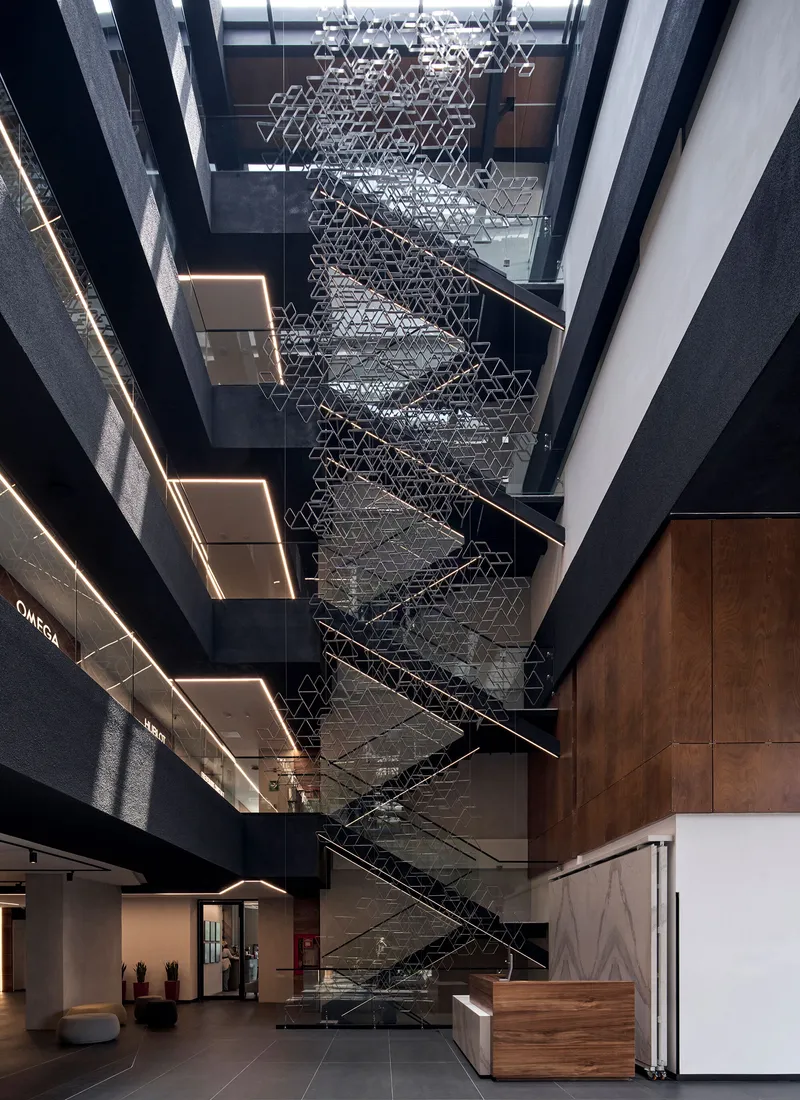 Multi-story atrium with geometric metal sculpture suspended above the central staircase and timber reception desk