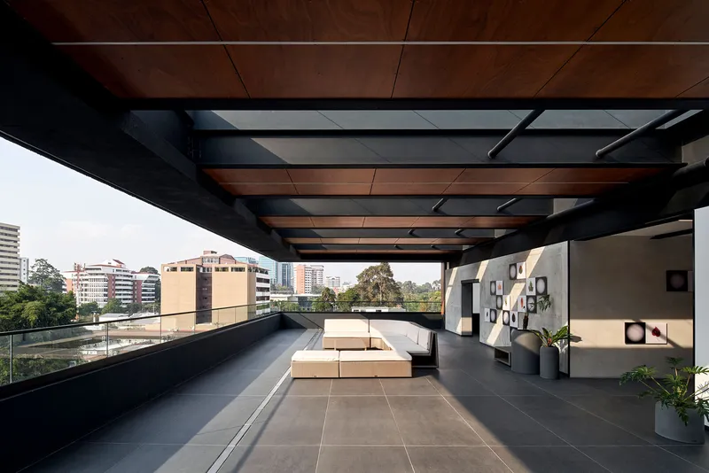 Rooftop terrace with exposed timber ceiling beams and dark steel frame overlooking the surrounding urban context