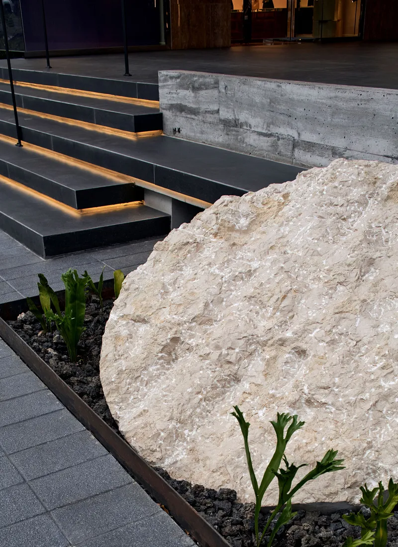 Textured limestone boulder beside planted bed with black steel stairs and integrated strip lighting
