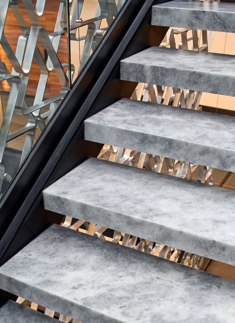 Concrete stair treads with black steel stringers and brass textured risers behind a glass balustrade