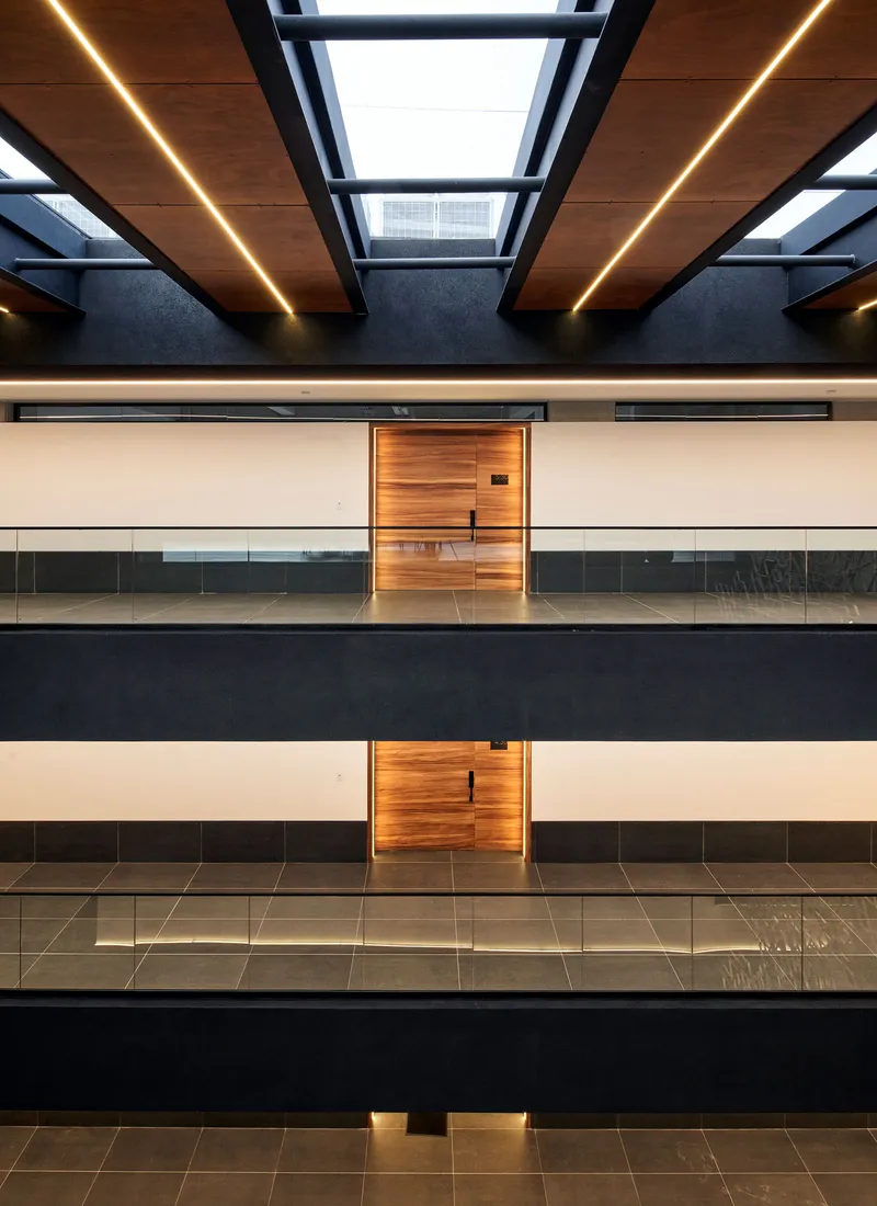 Symmetrical view of timber doors and glass balustrades across four levels beneath a skylit ceiling