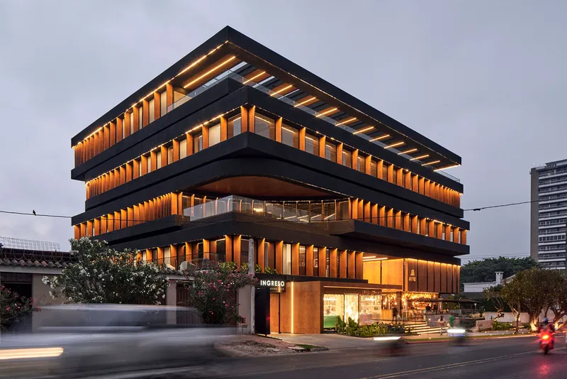 Corner view showing the terraced facade with illuminated timber fins and ground-level retail at twilight