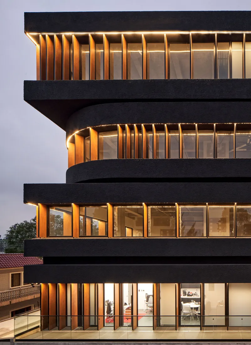 Detail of the cantilevered floor slabs with vertical timber fins between dark horizontal bands at dusk