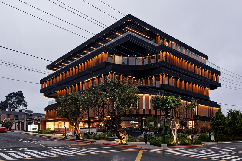 Street corner view of the illuminated building with mature trees and pedestrian crossing in foreground