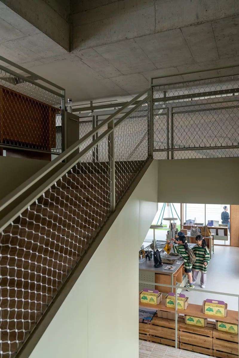 Staircase with mesh balustrades and exposed concrete ceiling overlooking a children's play area below