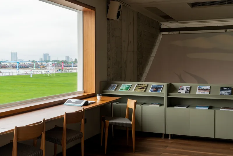 Reading table with timber chairs beside a window overlooking green lawn and waterfront beyond