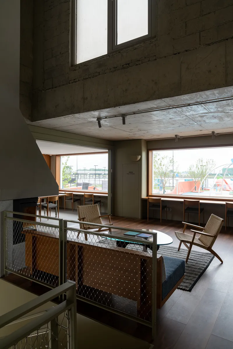 Mezzanine lounge with woven chairs and angled windows framing views of outdoor terrace and trees