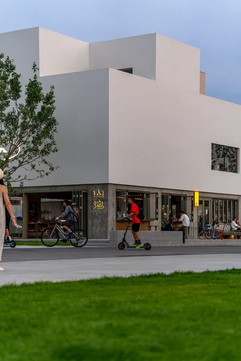 Street view of stacked white volumes above ground-floor retail with cyclists and pedestrians
