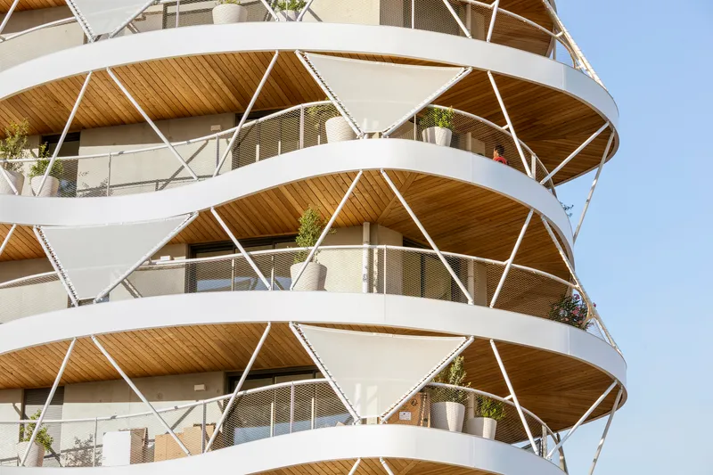 Close-up of the helical balcony structure with timber soffits and white steel bracing carrying potted plants
