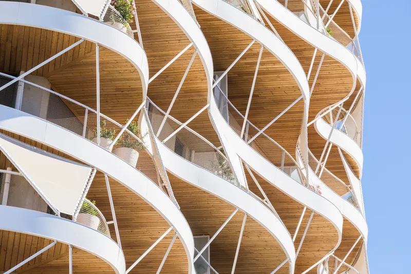 Detail of the criss-crossing white structural exoskeleton wrapping the curved balconies with timber ceilings