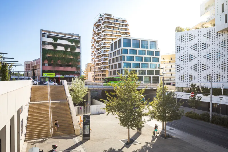 Plaza view with pedestrians and trees showing the tower among neighboring buildings in late afternoon