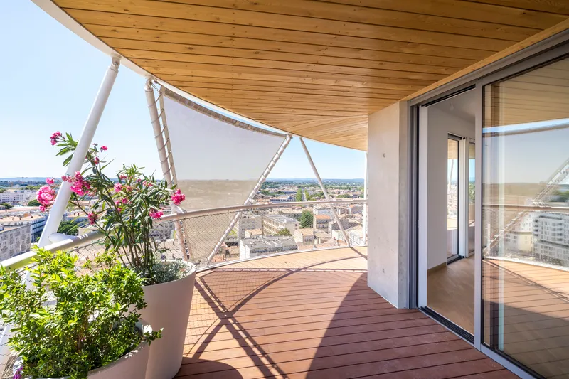 Timber-decked balcony with planted pots and tensile fabric shade overlooking the rooftops at dusk