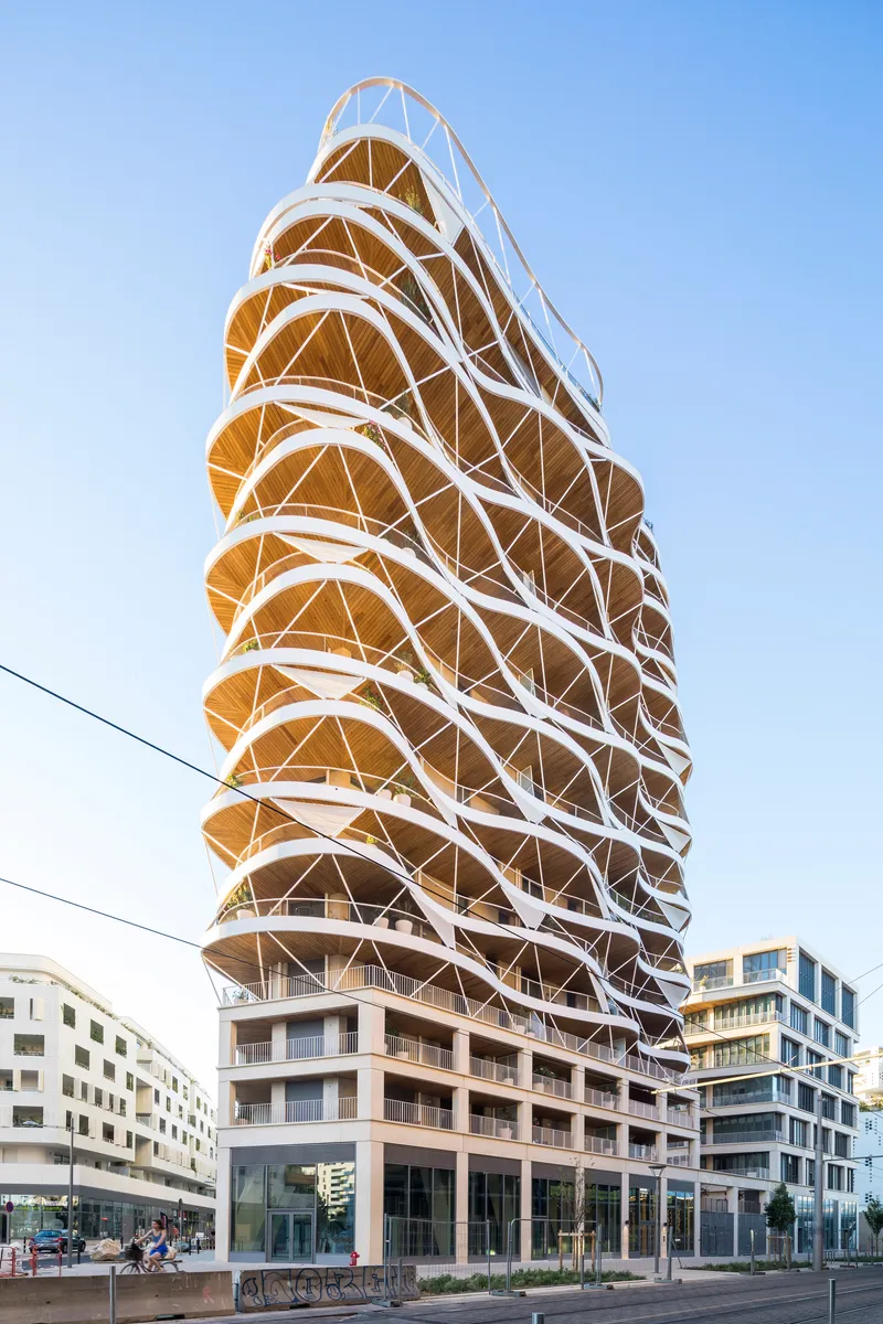 The helical tower facade with white diagonal bracing and timber-clad balconies seen from street level