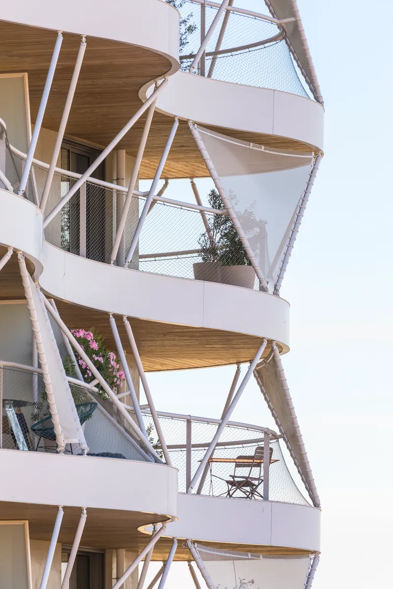 Close-up of stacked balconies with timber soffits, white diagonal struts, and mesh safety screens