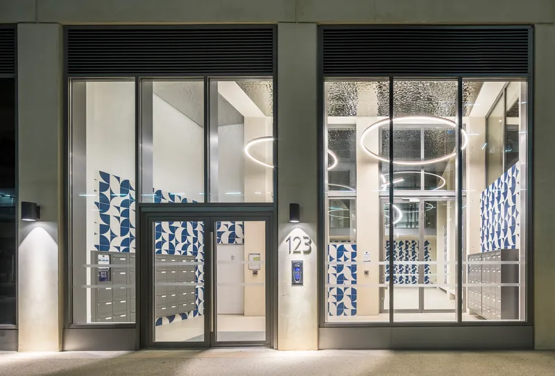 Glass entry lobby doors with integrated letterboxes and blue patterned tile panels at night