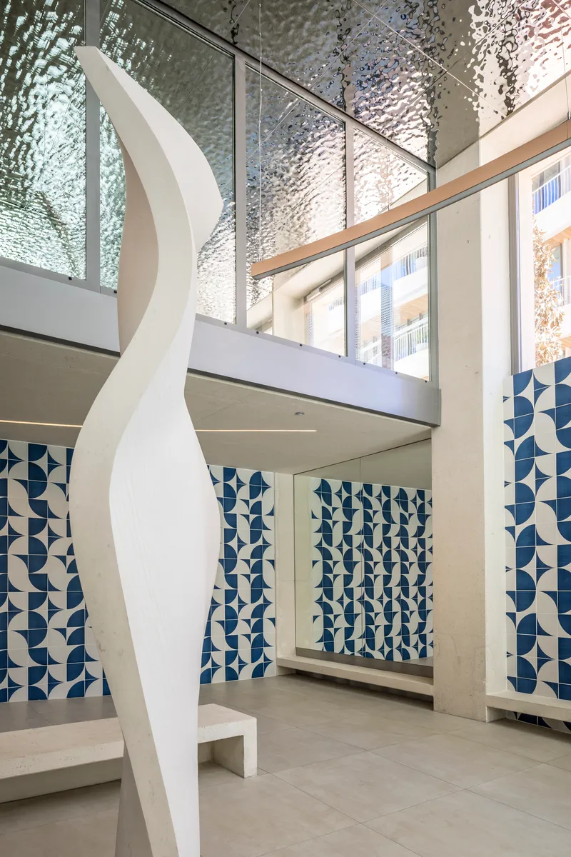 Double-height lobby with textured glass screens, blue tile wall panels, and white sculptural element