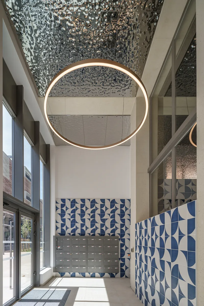 Double-height lobby with circular brass pendant light beneath a perforated metal ceiling and blue geometric tiled wall