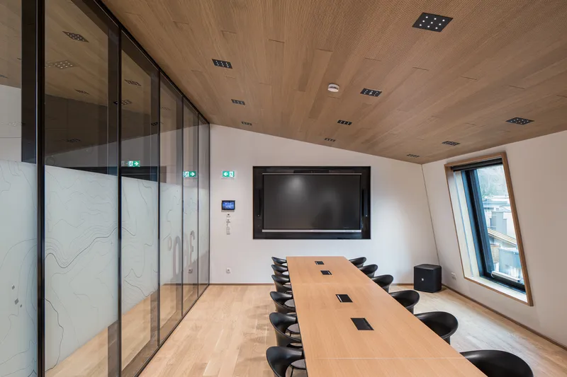 Conference room with timber ceiling, long table with black chairs and a wall-mounted screen