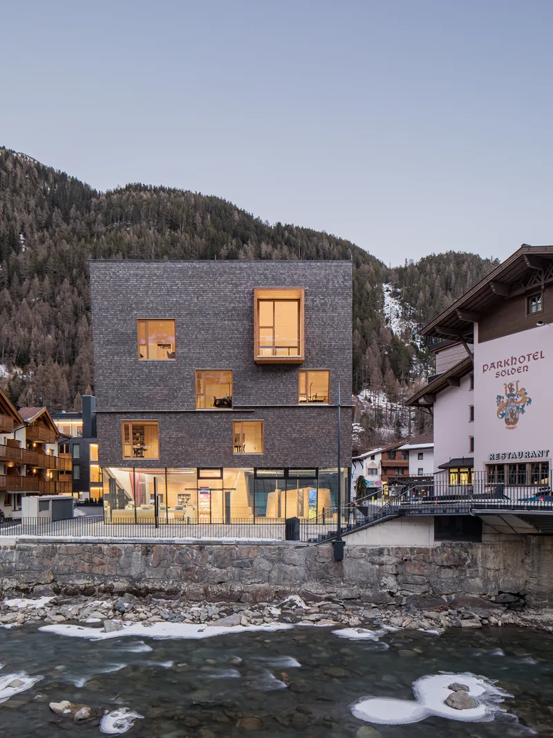 Dark slate shingle facade with illuminated windows overlooking a rushing river at dusk