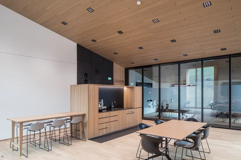 Break room with kitchenette, high tables and glass partition under continuous timber ceiling panels