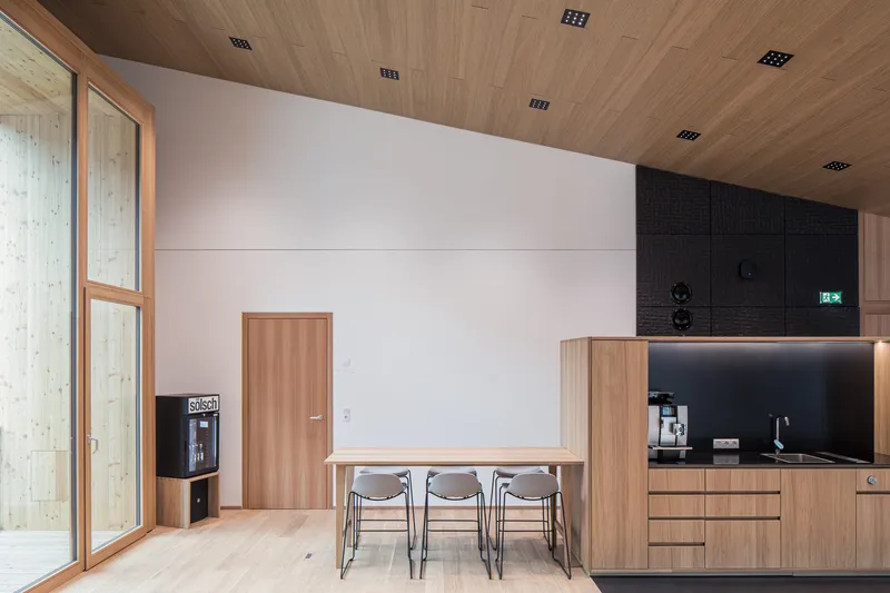 Timber dining table with grey chairs beside wood door and coffee bar under slatted ceiling