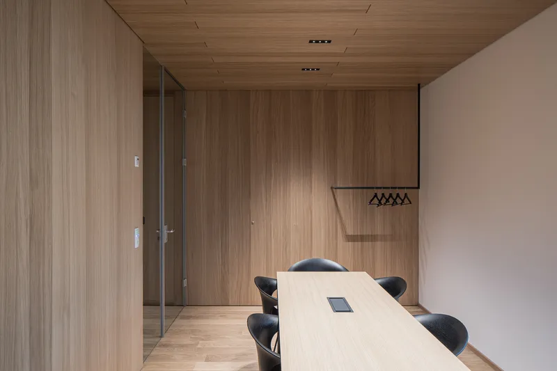 Conference room with timber-clad walls and ceiling, glass doors, and a light wood table with dark chairs