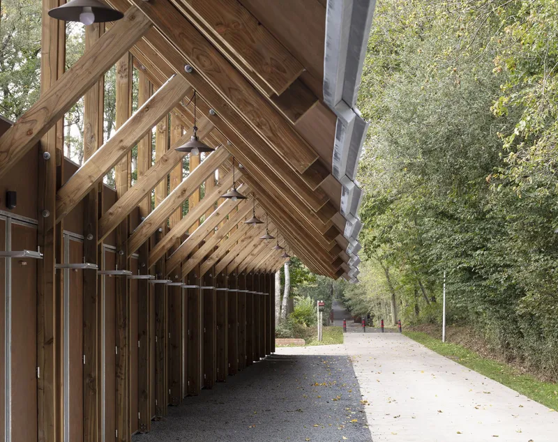 Covered walkway with exposed timber rafters and bronze metal wall panels flanking a gravel path