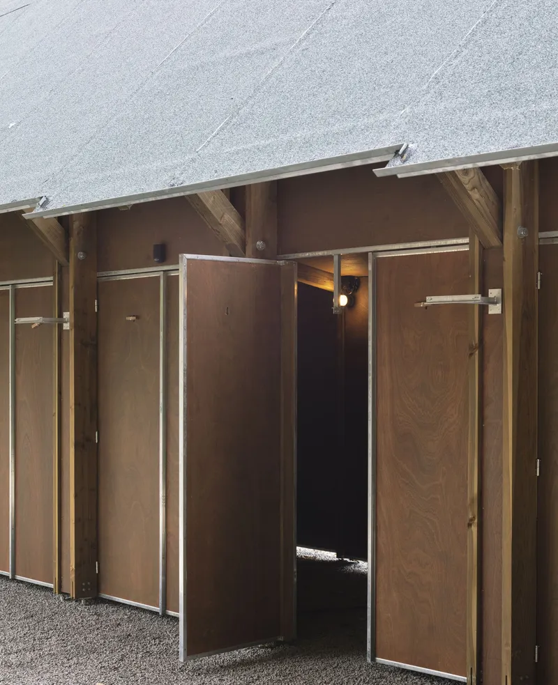 Close-up of timber-framed doorways with plywood panels and metal edging beneath a pitched gravel roof