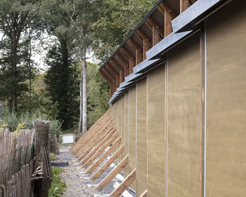 Angled timber bracing and canvas panels supporting the sloped roof overhang in a wooded setting